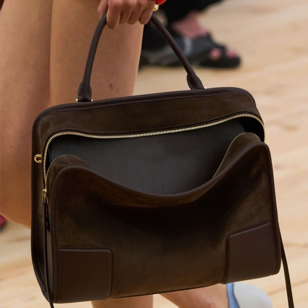 Brown leather bag held by a person on a blurred background