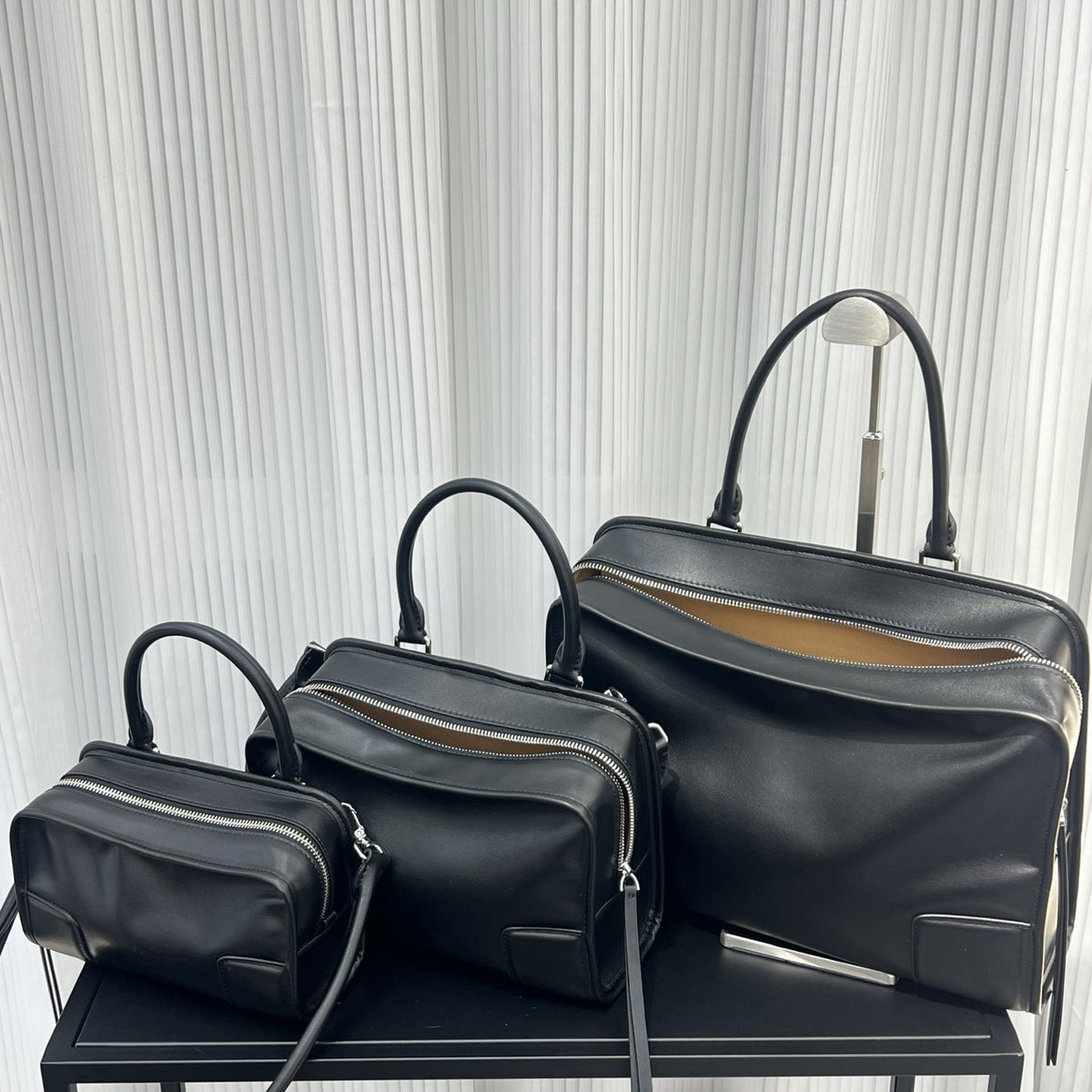 Three black handbags of varying sizes on a black surface with a light gray textured background