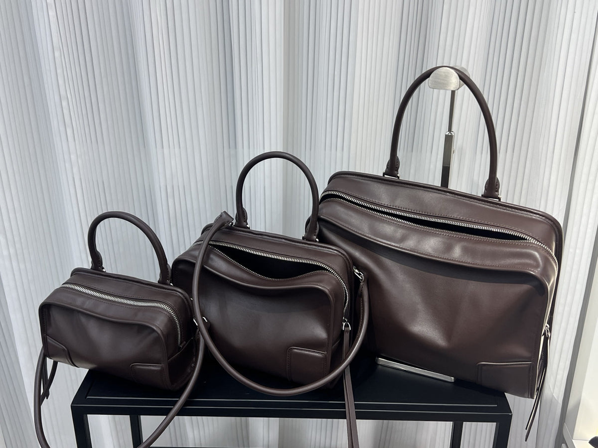 Three brown leather bags of different sizes on a black stand with a light gray curtain background.