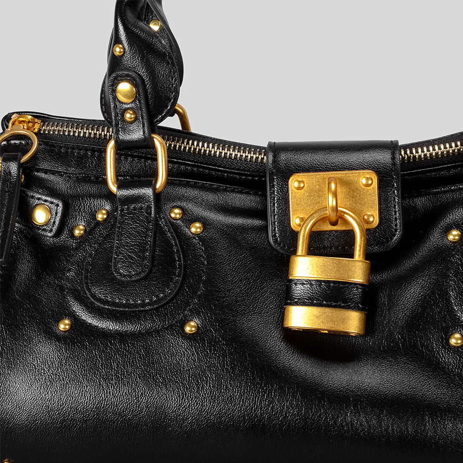 Black leather handbag with gold hardware on a light gray background