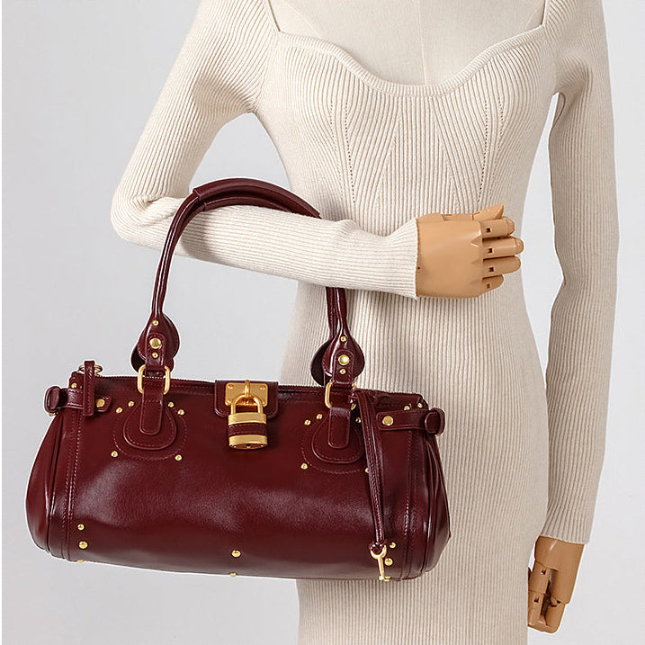 Brown handbag with gold accents held by a mannequin wearing a beige sweater.