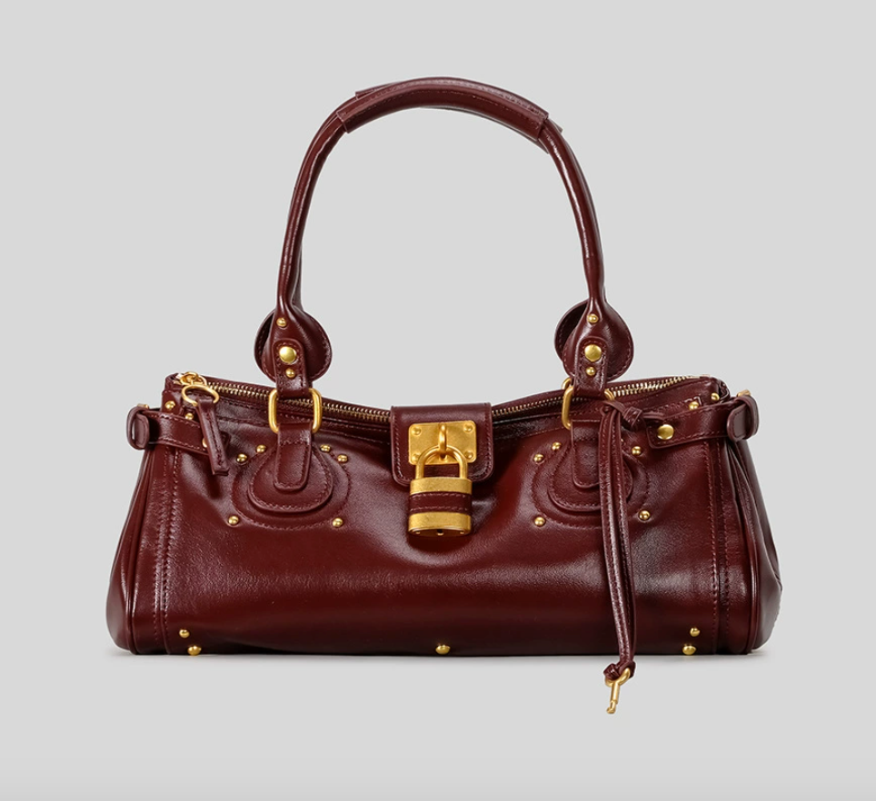 Brown leather handbag with gold accents on a light gray background