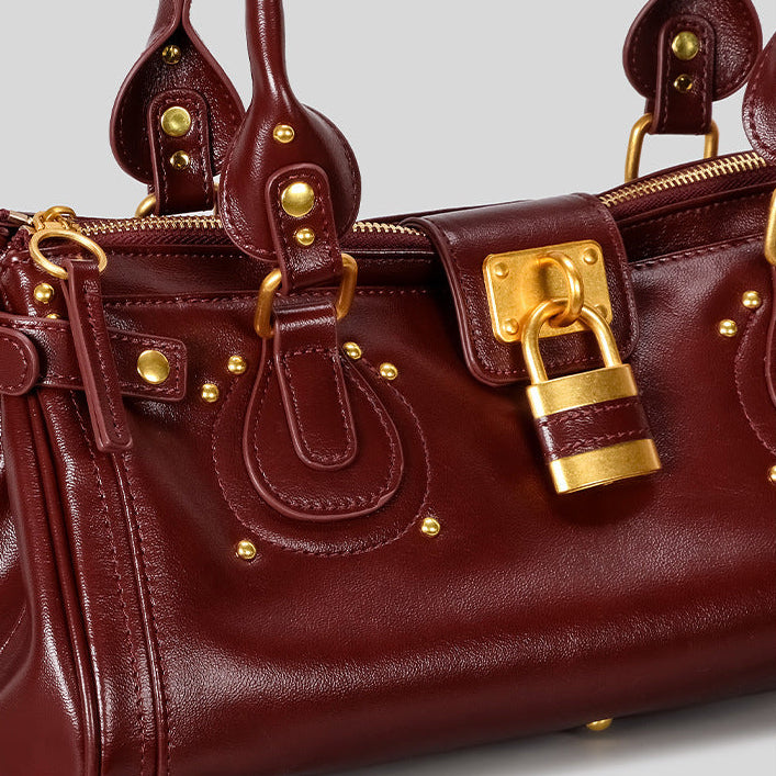 Burgundy leather handbag with gold hardware on a white background