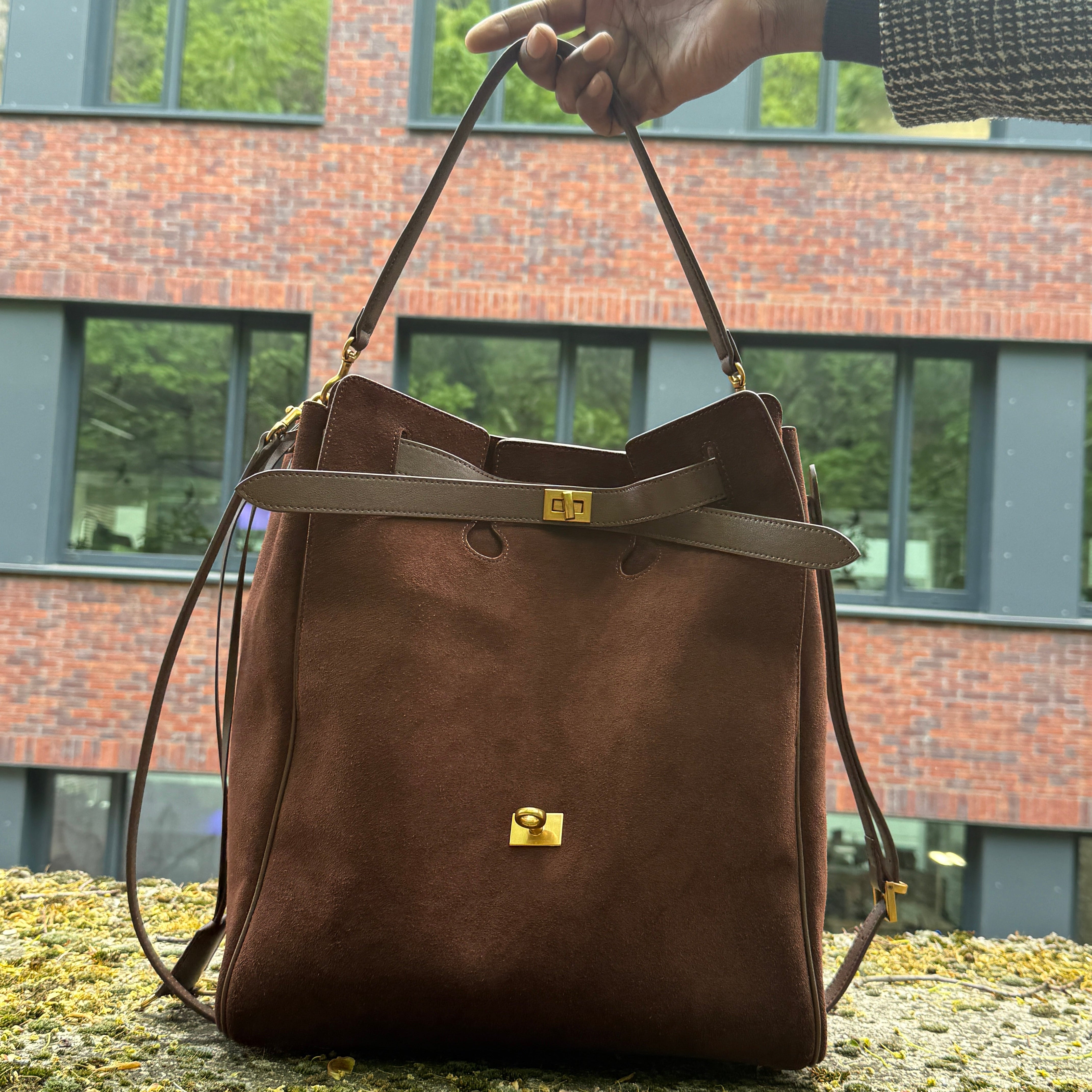 Brown leather bag being held against a brick building background