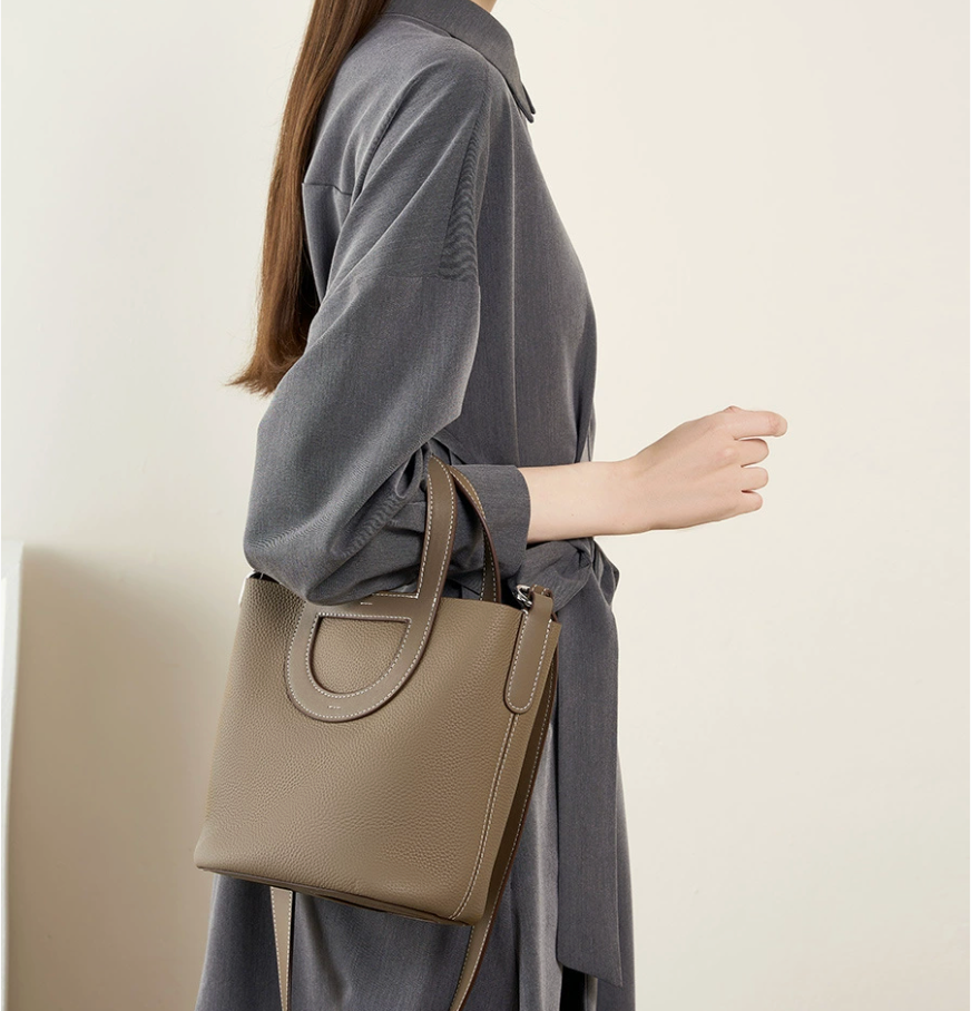 Person holding a beige handbag against a plain background