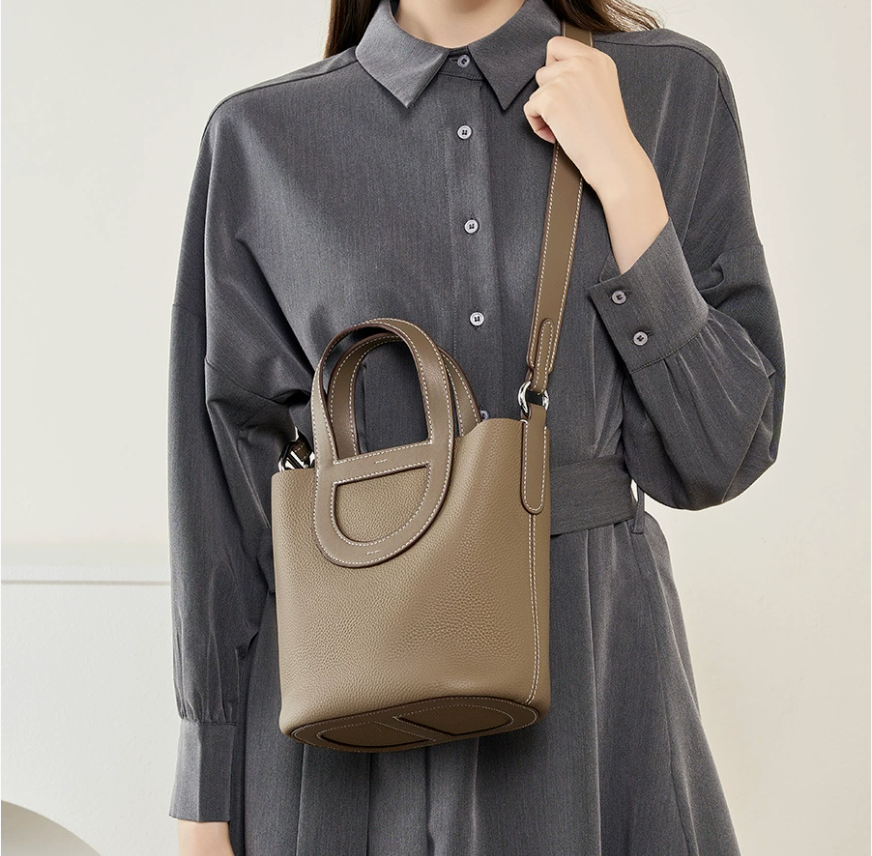 Person wearing a gray dress holding a beige handbag against a plain background