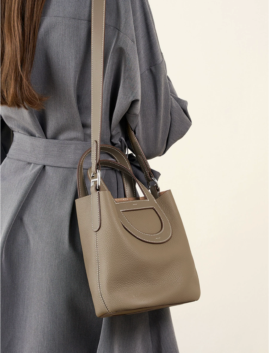 Person wearing a gray coat with a beige handbag on a plain background
