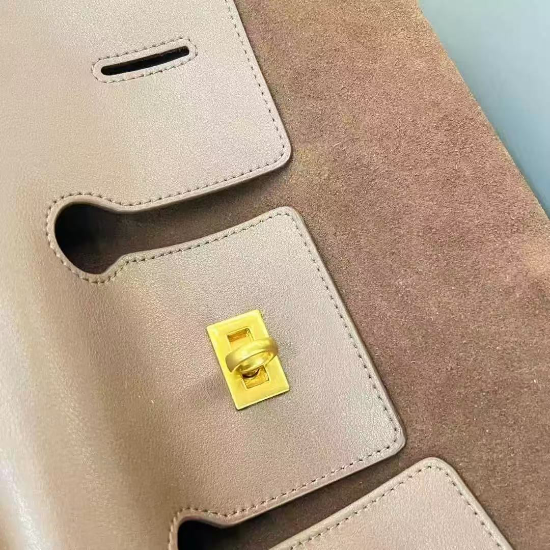 Close-up of a beige suede handbag with a gold clasp on a light blue background