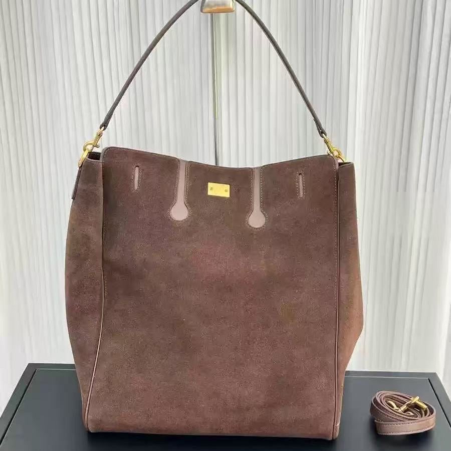 Brown suede handbag with gold accents on a black surface and white curtain background