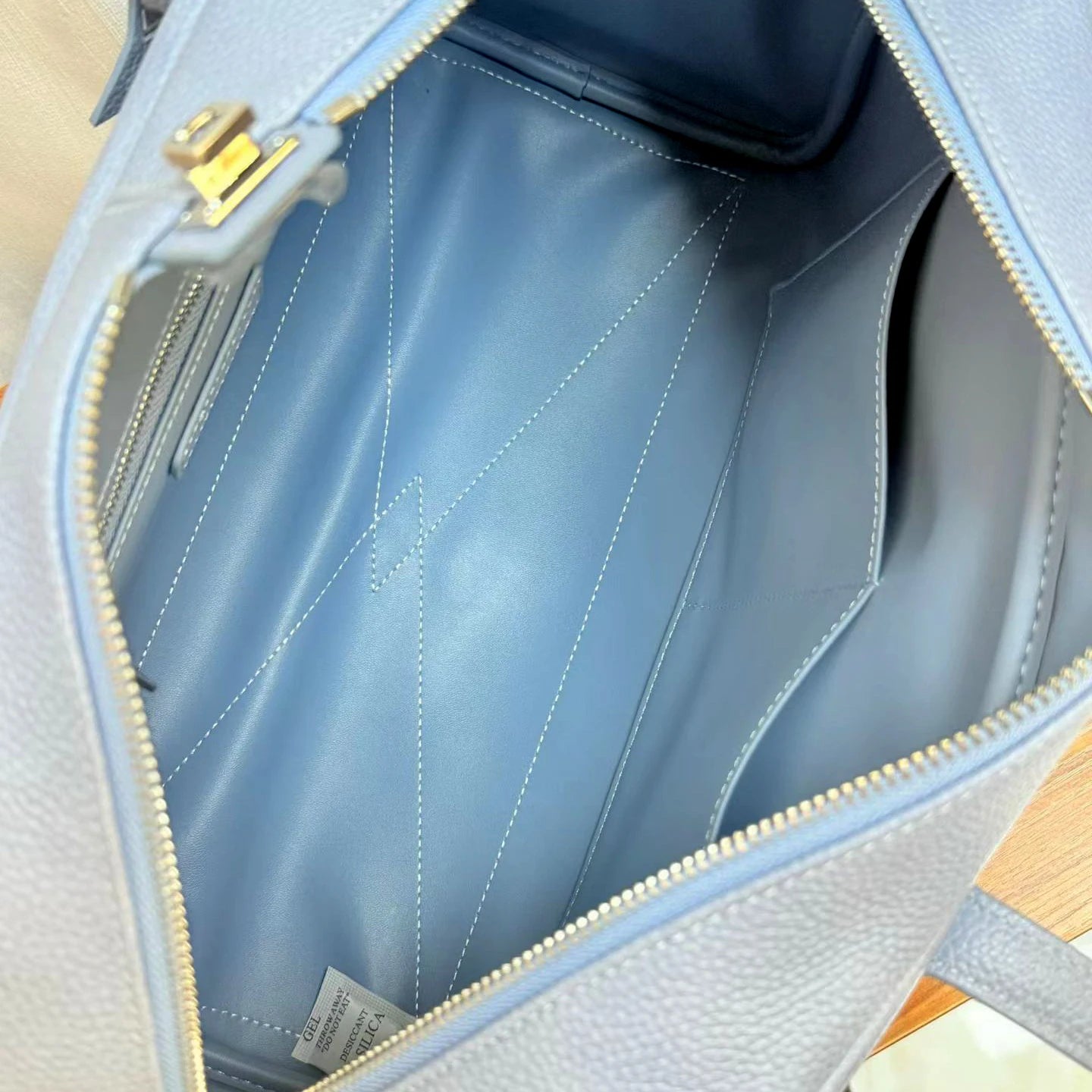 Close-up view of the interior of a light blue leather bag, showing the blue lining, white stitching, gold-tone zipper, and a small interior label.