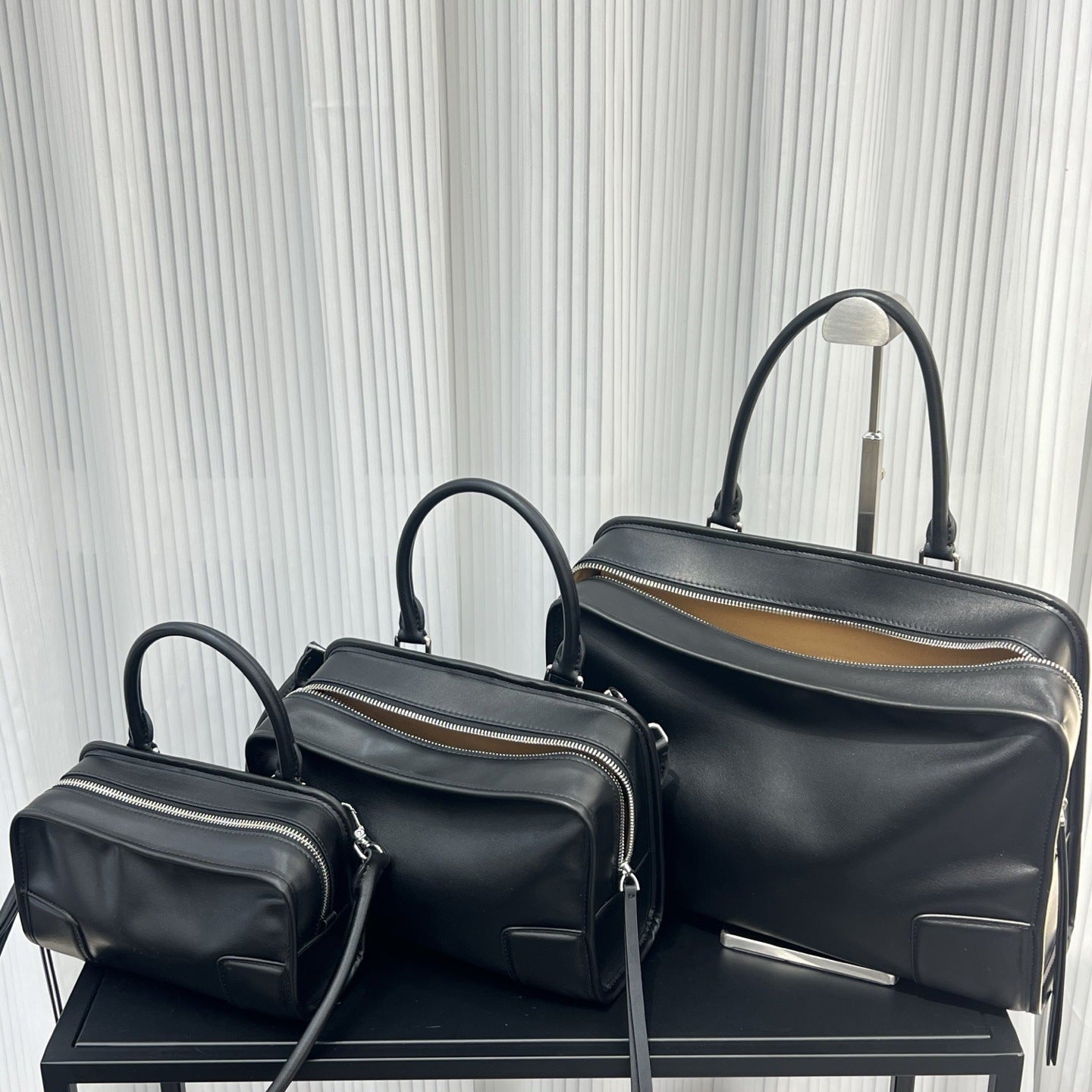 Three black handbags of varying sizes on a black surface with a light gray textured background