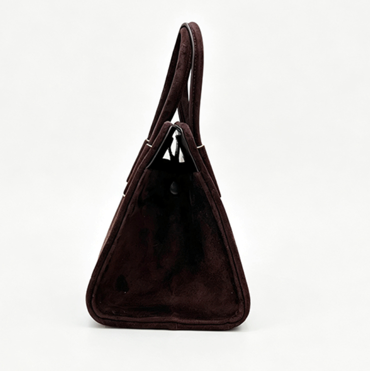 A dark brown suede handbag with a triangular silhouette and a single top handle, photographed from the side against a plain white background.