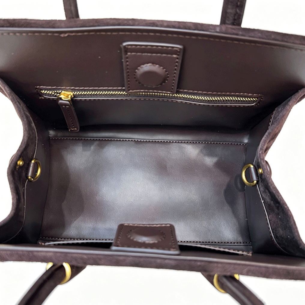 Close-up interior view of a dark brown leather handbag showing the spacious main compartment, a zippered pocket, and gold-tone hardware on a white background.