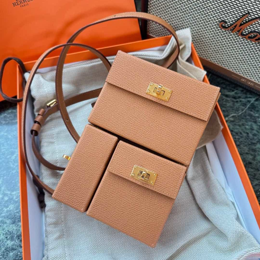 A tan textured leather crossbody bag with gold-tone hardware, presented inside an orange Hermès box with its dust bag and strap.